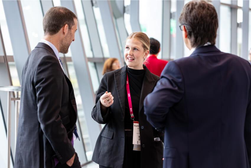 Three business professionals in conversation at a networking event, representing relationship-based franchise leadership.